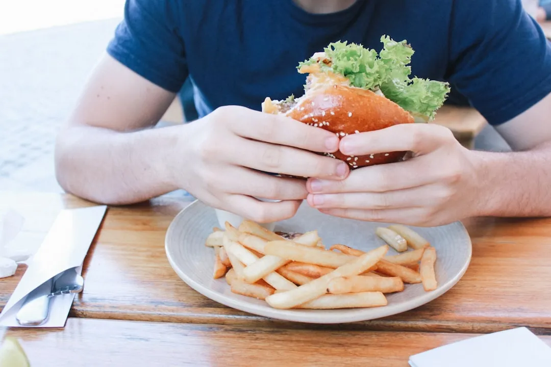 Pessoa comendo hambúrguer com batatas fritas no prato