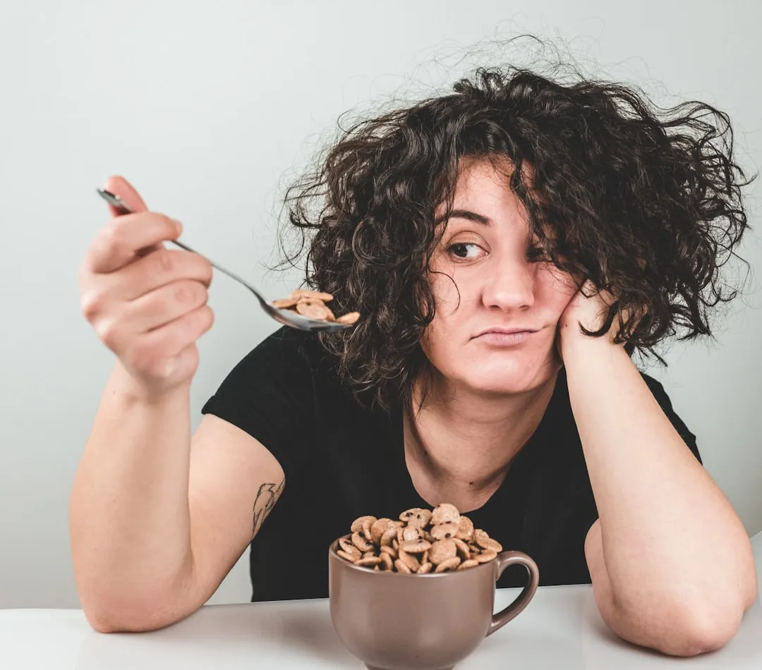 Mulher com cabelo bagunçado vestindo uma camiseta preta de gola alta, colher com cereais por cima Mulher com cabelo bagunçado vestindo uma camiseta preta de gola alta, colher com cereais por cima
