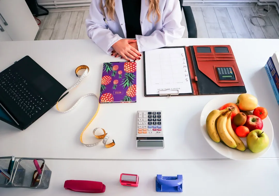 Uma mulher sentada à mesa com um prato de frutas e uma calculadora