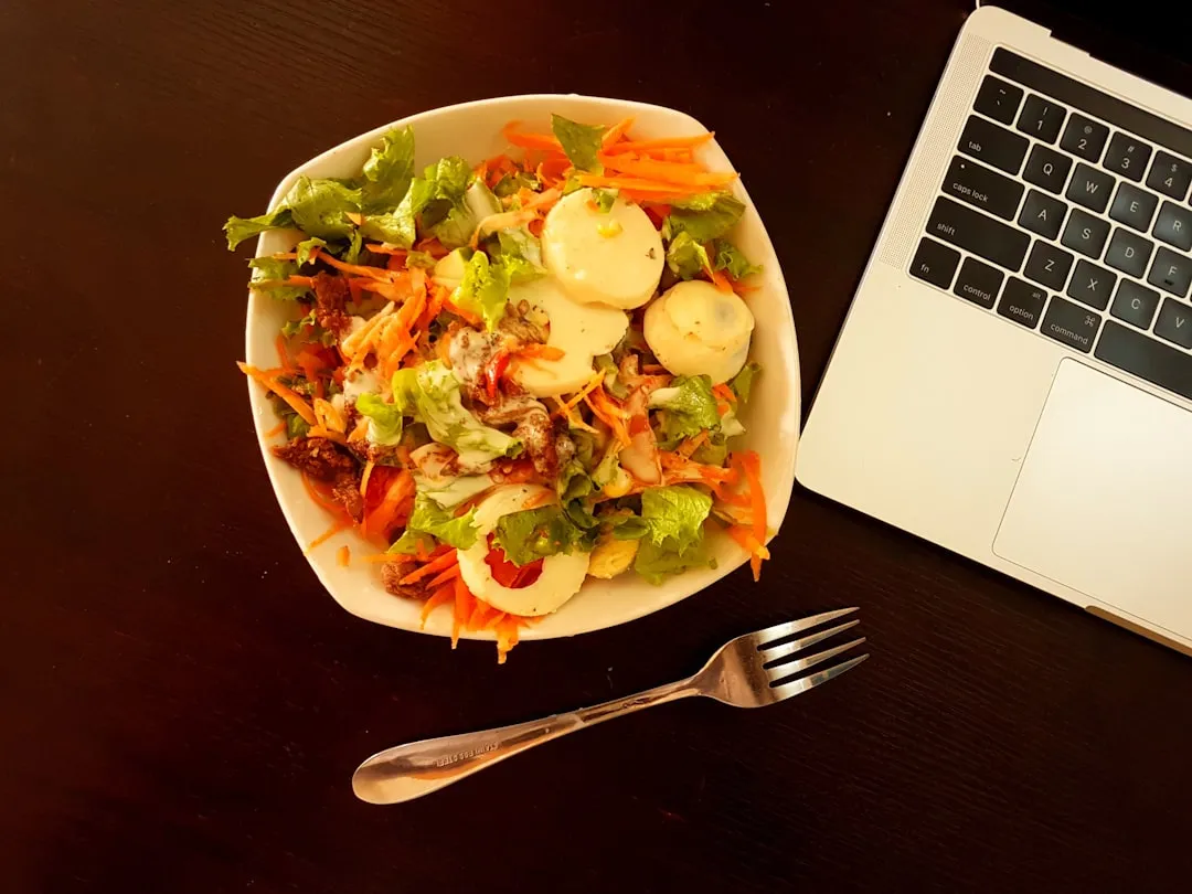 Tigela de cerâmica branca com salada de legumes ao lado do laptop cinza