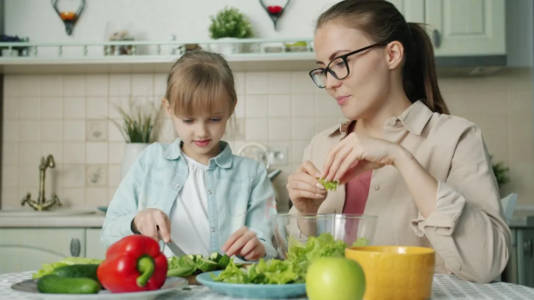 Mãe e filha preparando salada na cozinha.