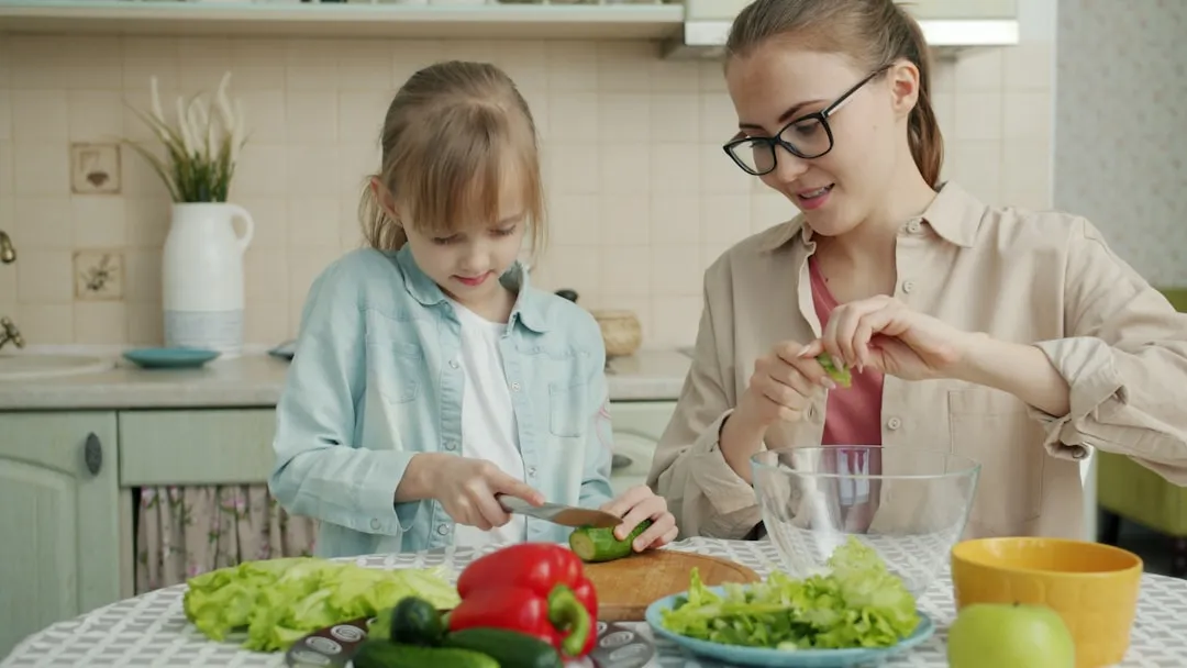 Mãe e filha preparando salada na cozinha.