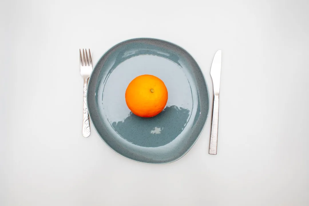 Uma laranja sentada em um prato com um garfo e uma faca